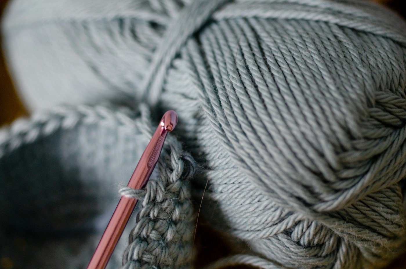 Pink crochet hook, a crochet swatch, and pale gray yarn.